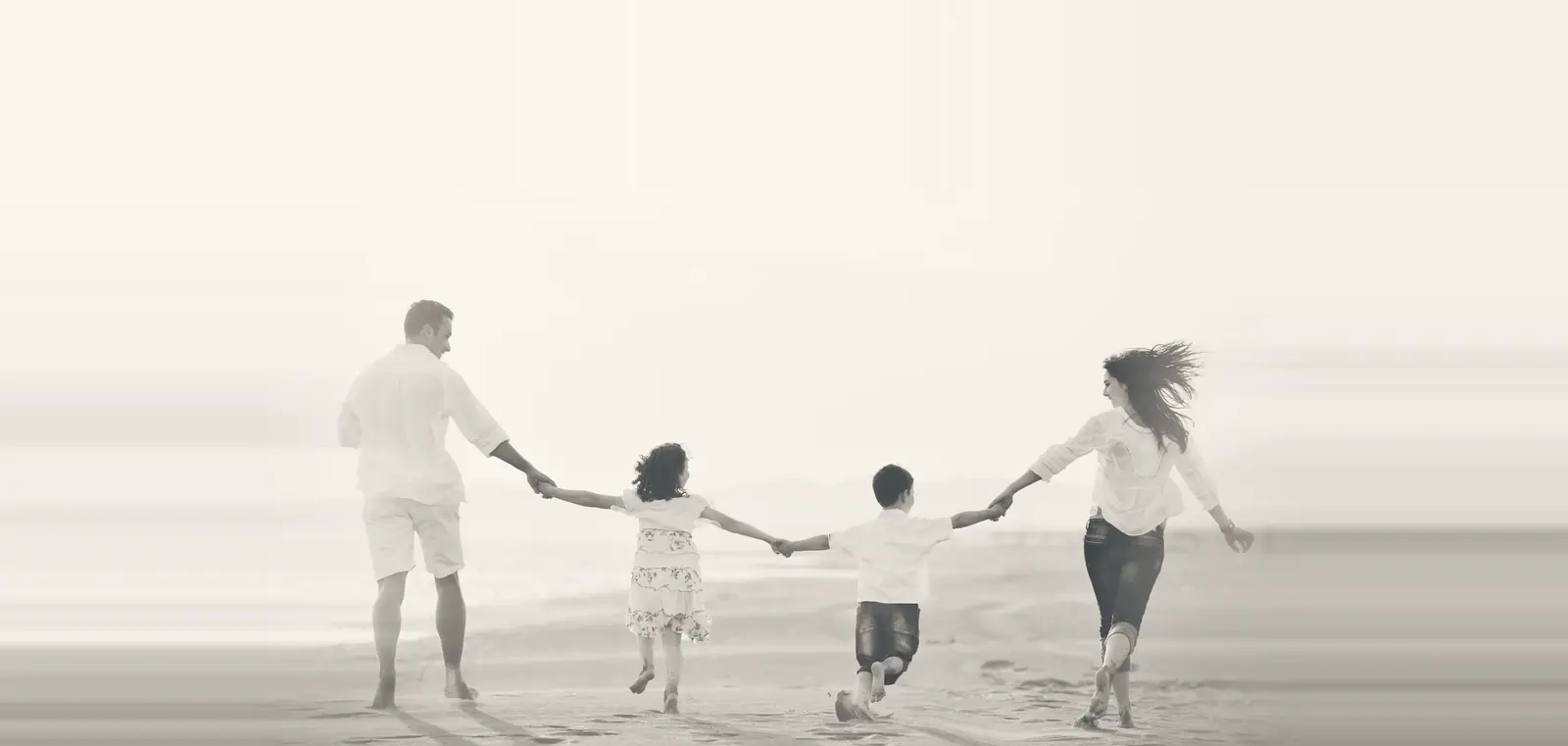 A family of four holding hands as they run along the beach